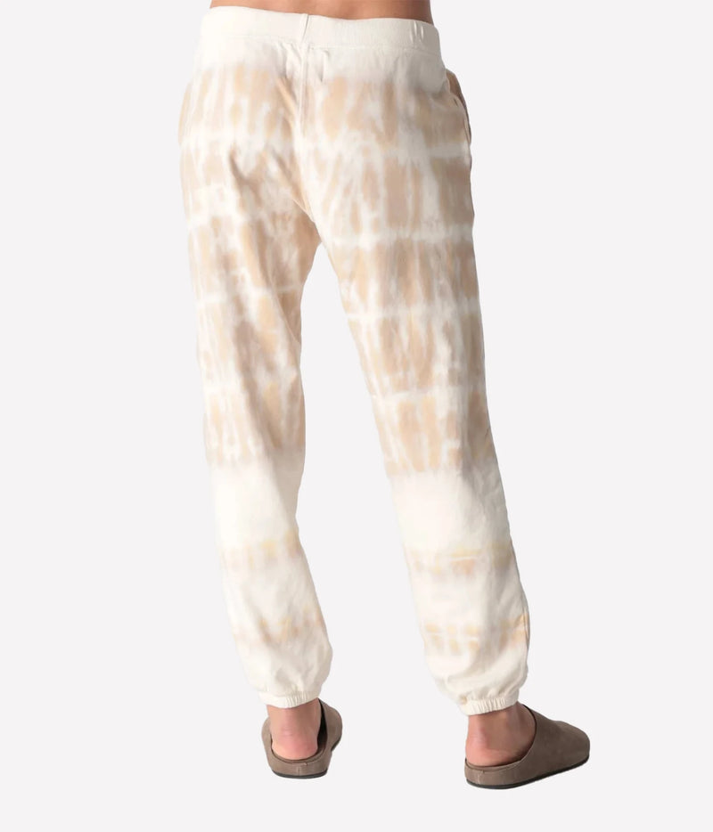 Back view of a model wearing the Electric Rose Classic Horizon Jogger in Dune Ivory, showing the relaxed fit and the tie-dye fading towards the cuffed hem, with taupe suede clogs