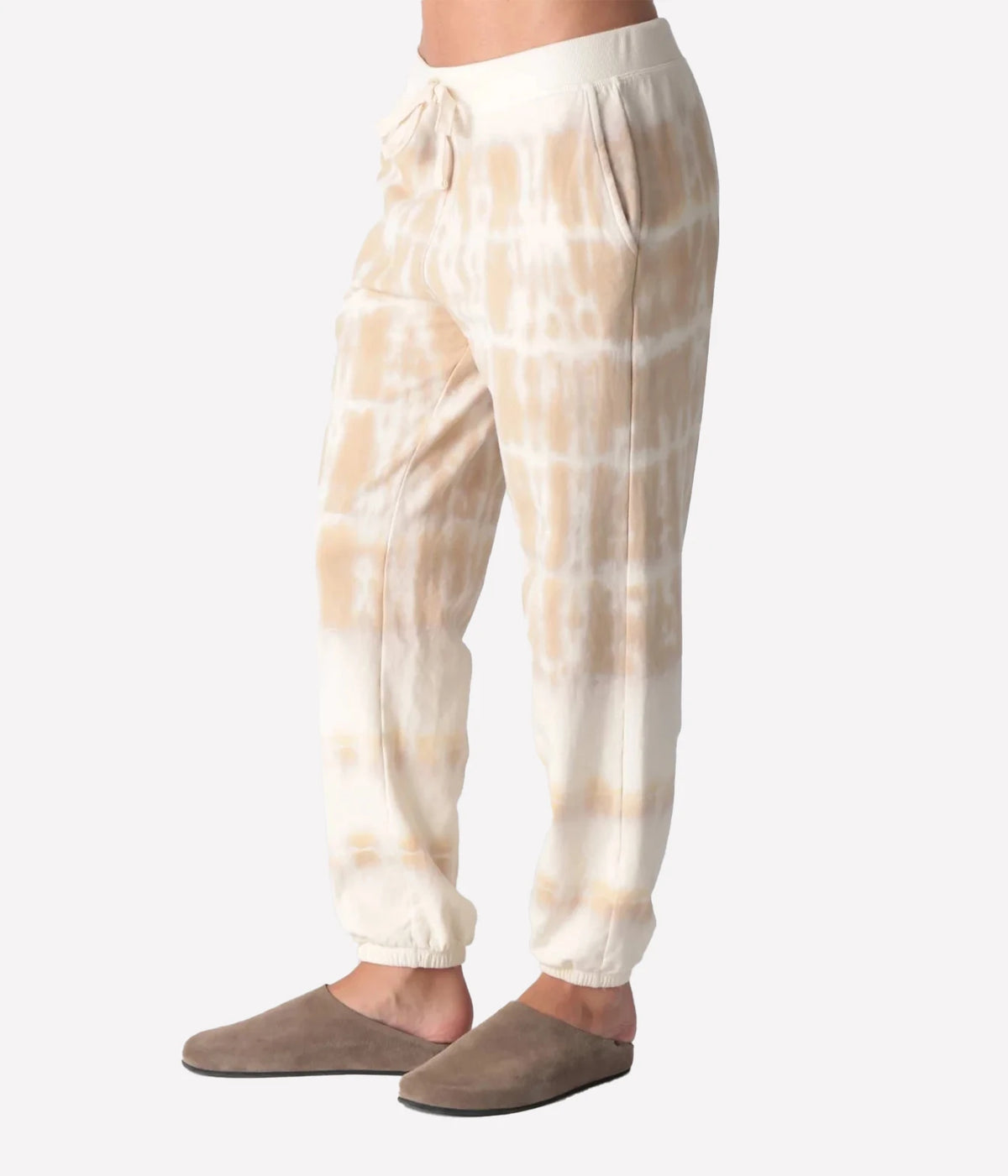 Side profile of a model wearing the Electric Rose Classic Horizon Jogger in Dune Ivory, showing the side pocket and relaxed leg tapering to elasticated cuffs, with taupe suede clogs