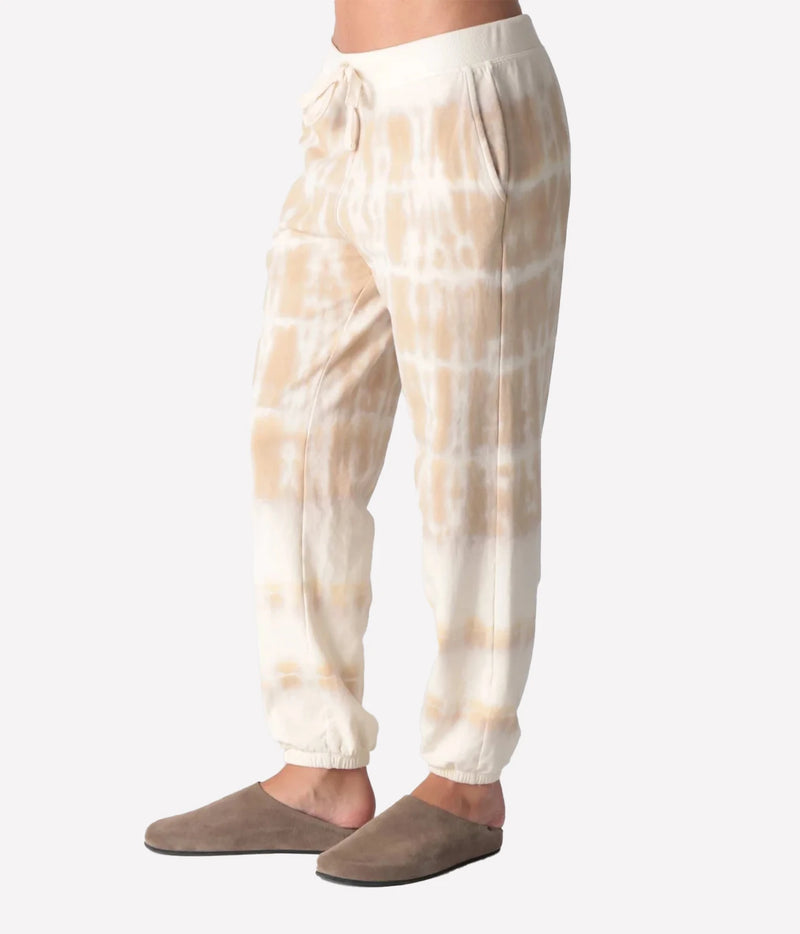 Side profile of a model wearing the Electric Rose Classic Horizon Jogger in Dune Ivory, showing the side pocket and relaxed leg tapering to elasticated cuffs, with taupe suede clogs
