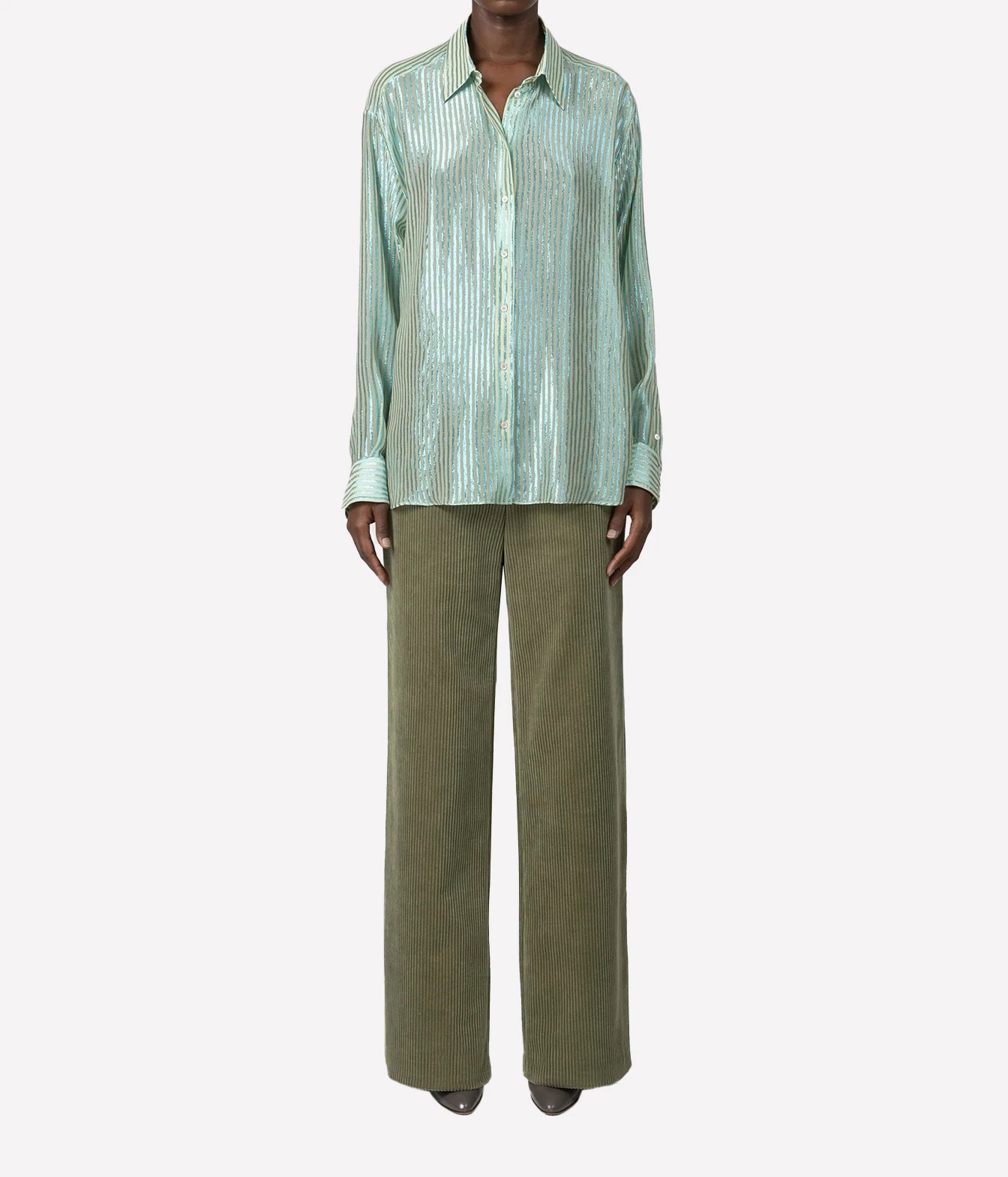 A model wearing a light mint green metallic pleated button-down shirt and olive green wide-leg trousers, shown against a plain light gray background.