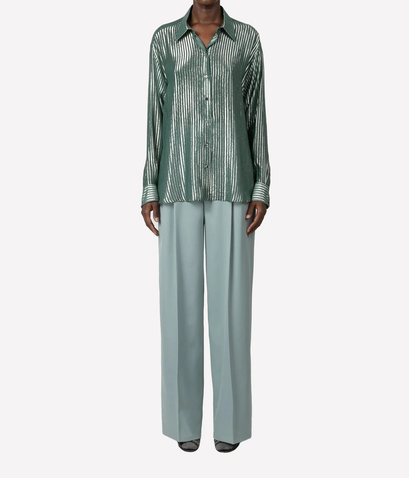 A model wearing a green and white vertically striped button-down shirt paired with light sage green wide-leg trousers, shown against a plain light gray background.