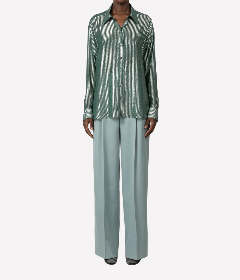 A model wearing a green and white vertically striped button-down shirt paired with light sage green wide-leg trousers, shown against a plain light gray background.