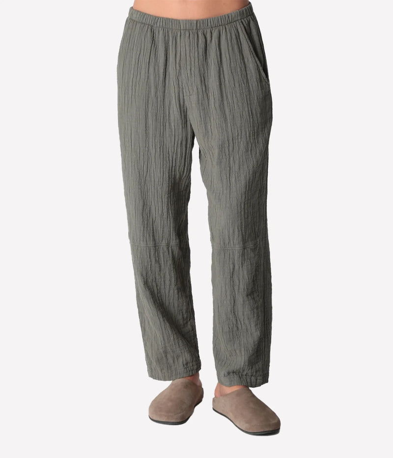 Front view of a model wearing the Electric Rose Kick Back Pant in Moss, showing the crinkled texture, elastic waistband, side pockets and relaxed straight leg, with taupe suede clogs