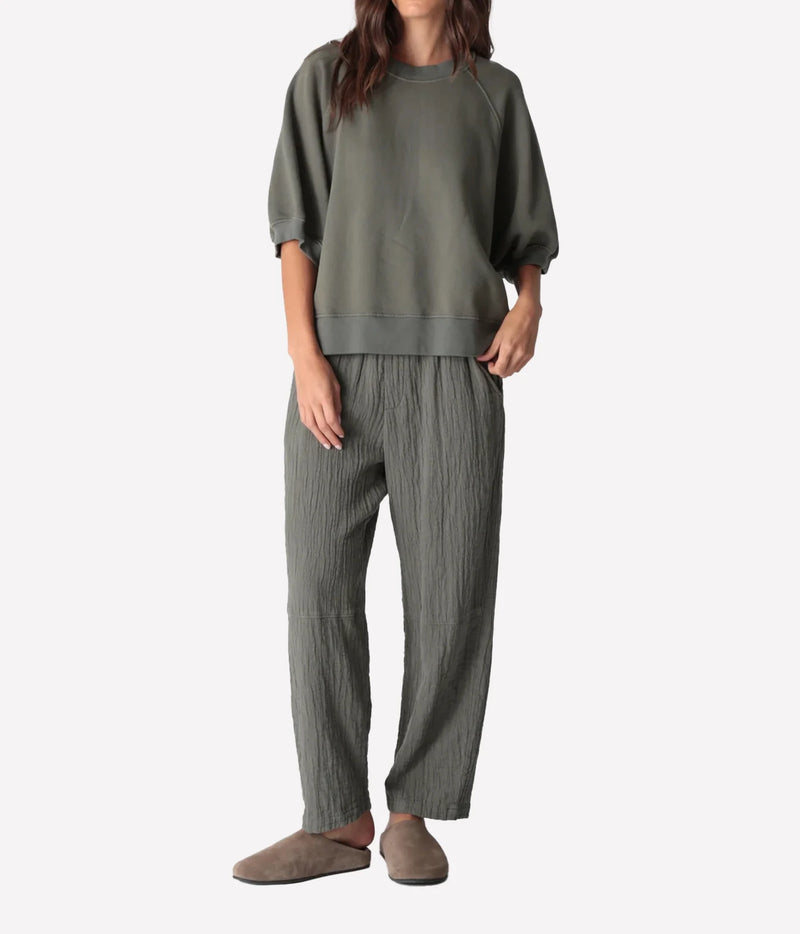 Full-length front view of a model wearing the Electric Rose Kick Back Pant in Moss with a matching moss green short-sleeve sweatshirt and taupe suede clogs