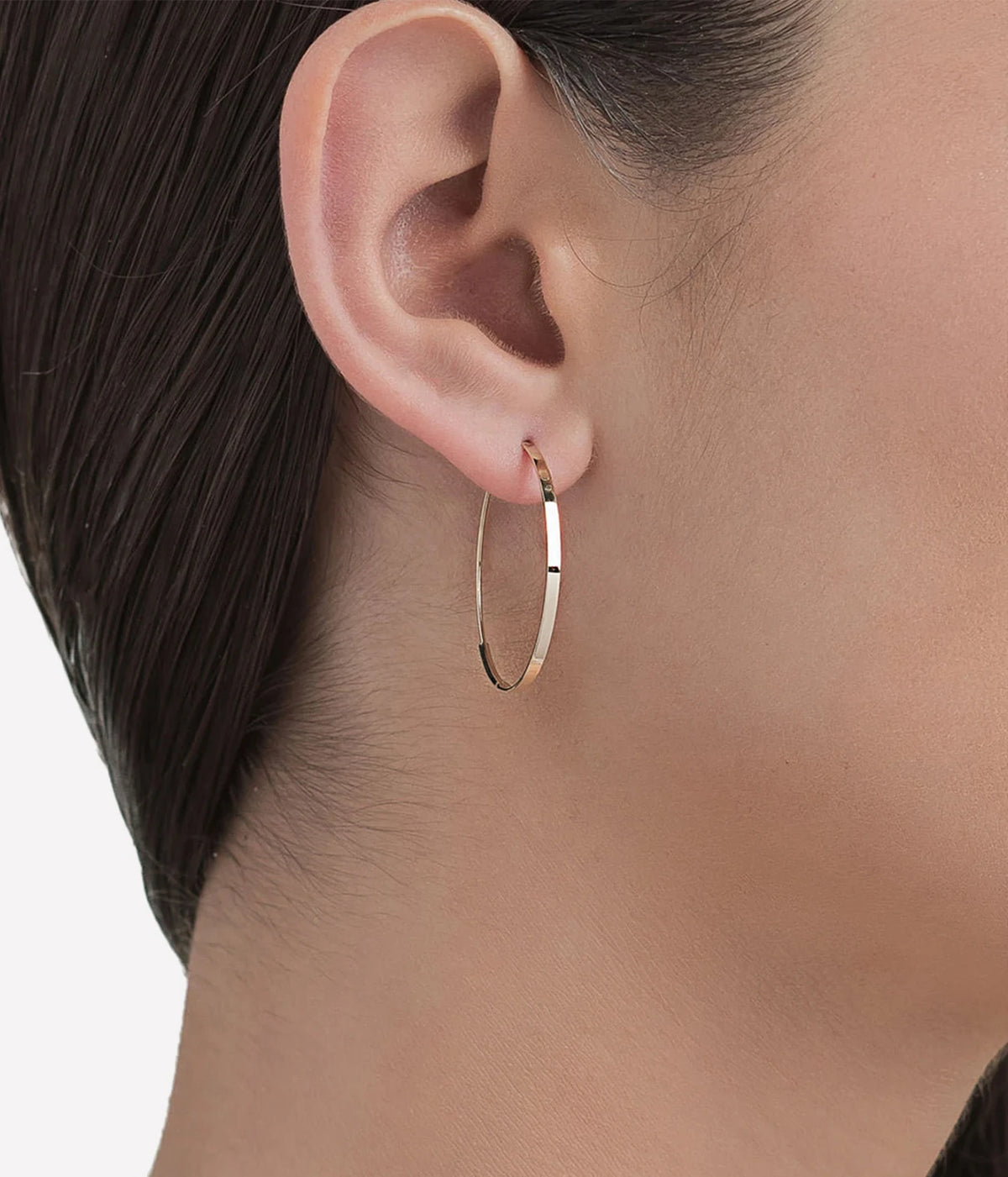 Close-up of a model wearing the LANA Small Flat Magic Hoops in Yellow Gold, showing the slim round hoop sitting close to the ear