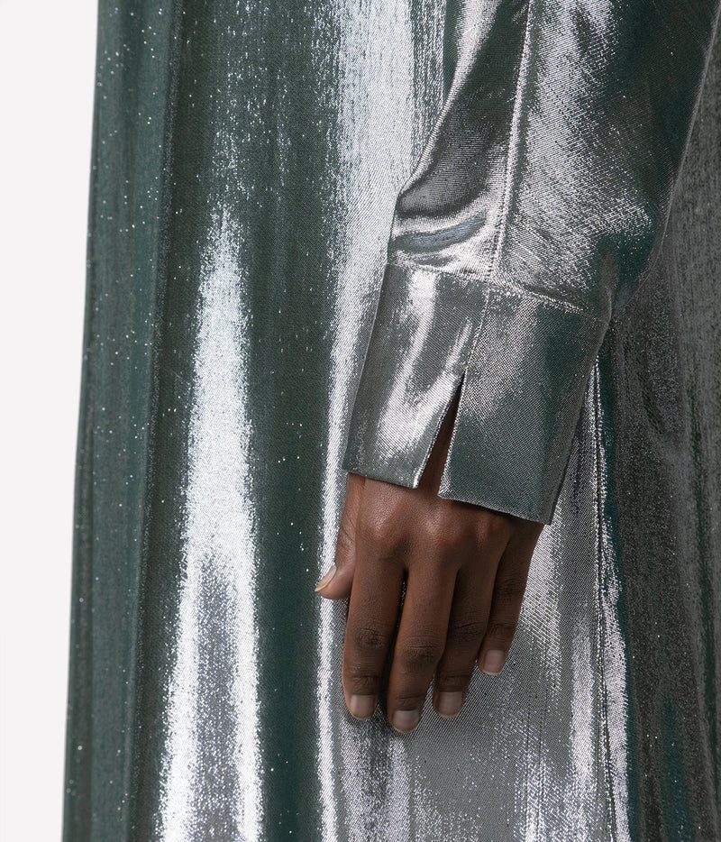 A close-up of a person's hand resting on a shimmering, metallic sage green fabric garment with a matching sleeve featuring a cuff slit.