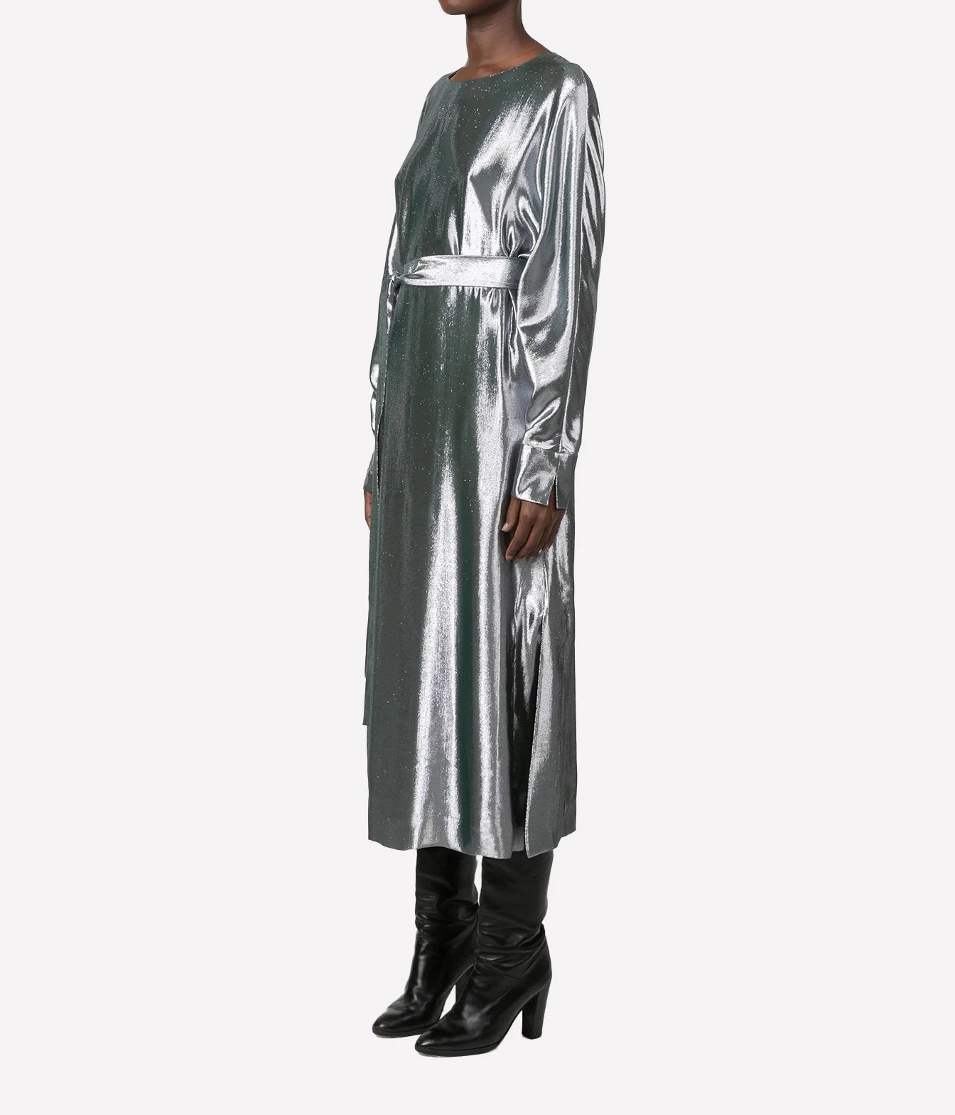 A model wearing a long-sleeved metallic silver midi dress with a matching waist belt, paired with black leather knee-high boots, set against a plain light gray background.