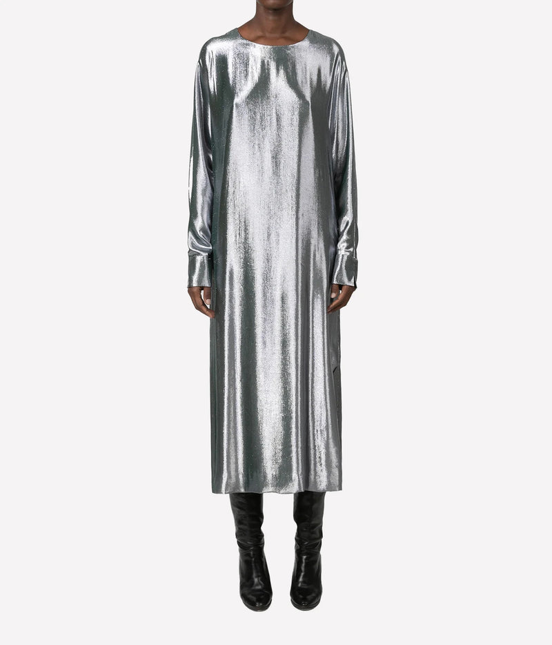 A model wearing a long-sleeved, midi-length metallic silver dress with a crew neck, paired with black knee-high boots, against a plain light gray background.