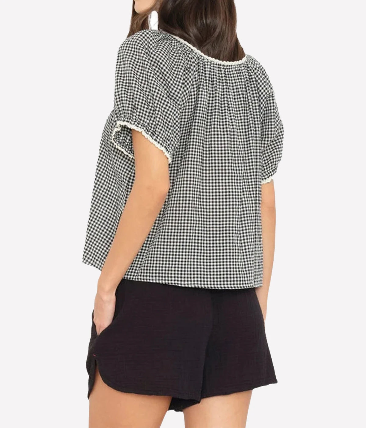 Back view of a model wearing the Xirena Maisie Top in Black Sand with black shorts, showing the gathered neckline with contrast trim and puff sleeves
