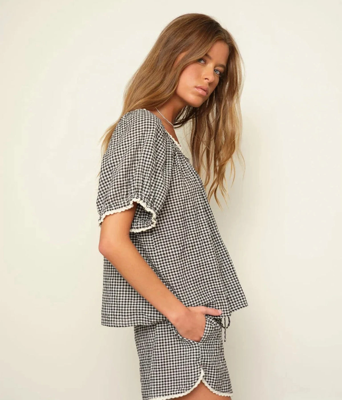 Side profile of a model wearing the Xirena Starla Short in Black Sand with the matching Maisie Top and one hand in the side seam pocket, showing the curved dolphin hem with contrast trim