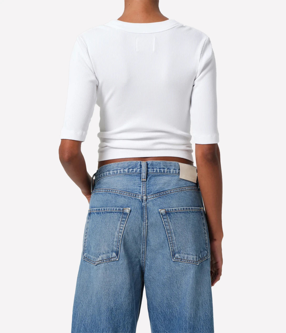 Person wearing a white cropped top and blue jeans on a plain background