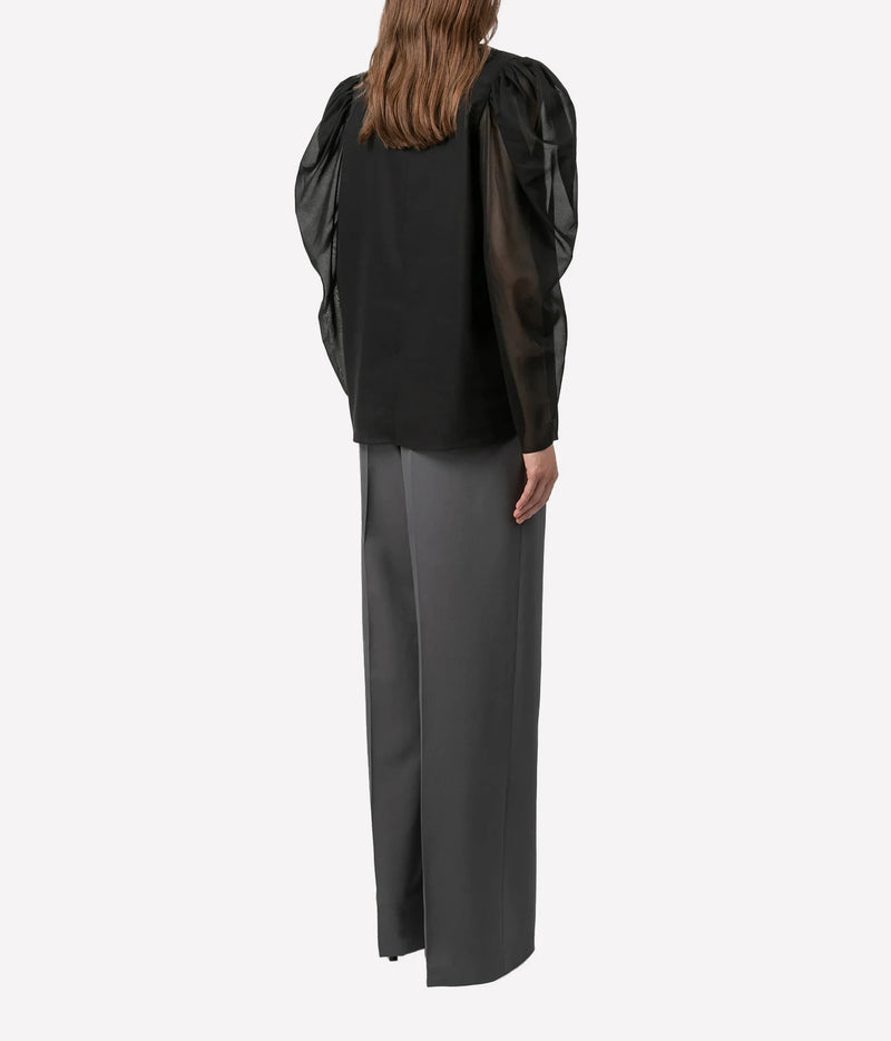 A model shown from the back wearing a black long-sleeve blouse with sheer puff sleeves and dark gray wide-leg trousers, set against a plain light gray background.