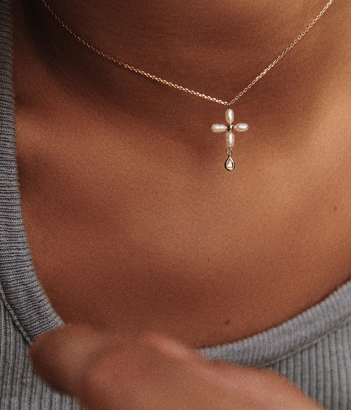 Close-up of a model wearing the Pascale Monvoisin Palerme White Pearl Necklace with a grey ribbed top, the pearl cross sitting at the base of the neck