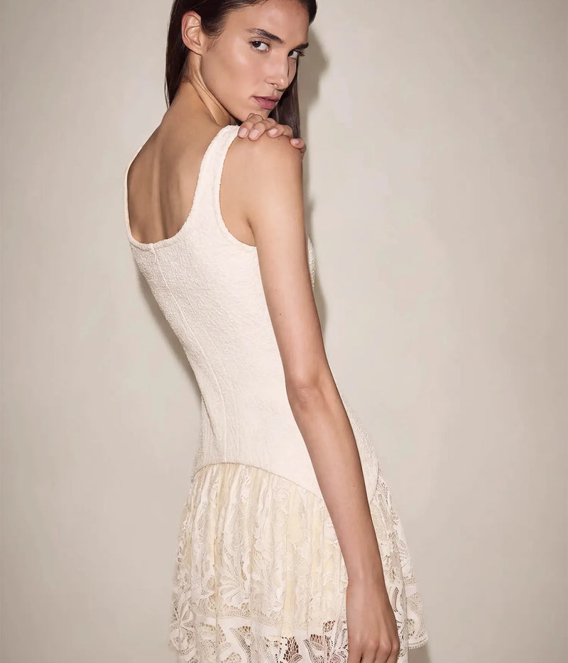 Back view of a model wearing the Alexis Pomela Mini Dress In Ivory looking over her shoulder, showing the tank straps, fitted textured back and layered lace hem