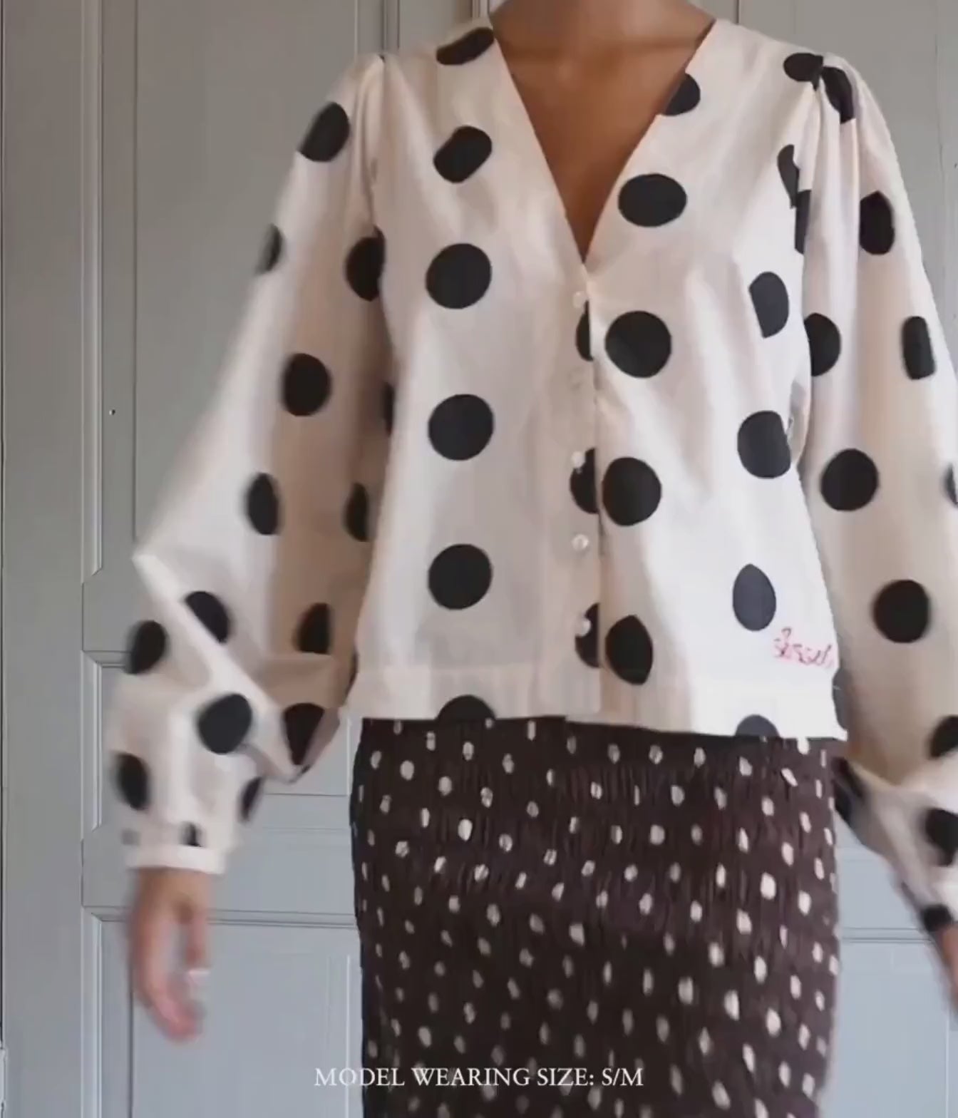 Model wearing the Sissel Edelbo Ea Shirt In Black Dot with brown polka dot skirt showing the V-neckline, balloon sleeves and cropped length