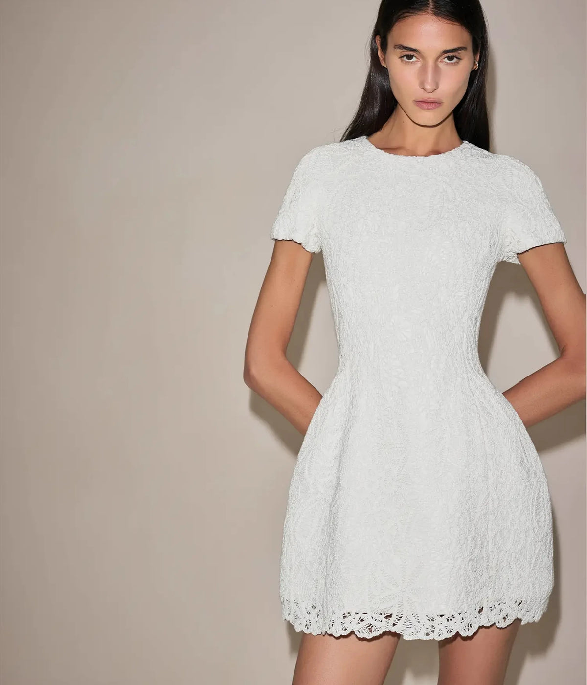 Front view of a model wearing the Alexis Regatta Dress In Floral Macrame with arms by her sides, showing the short sleeves, nipped-in waist and flared skirt
