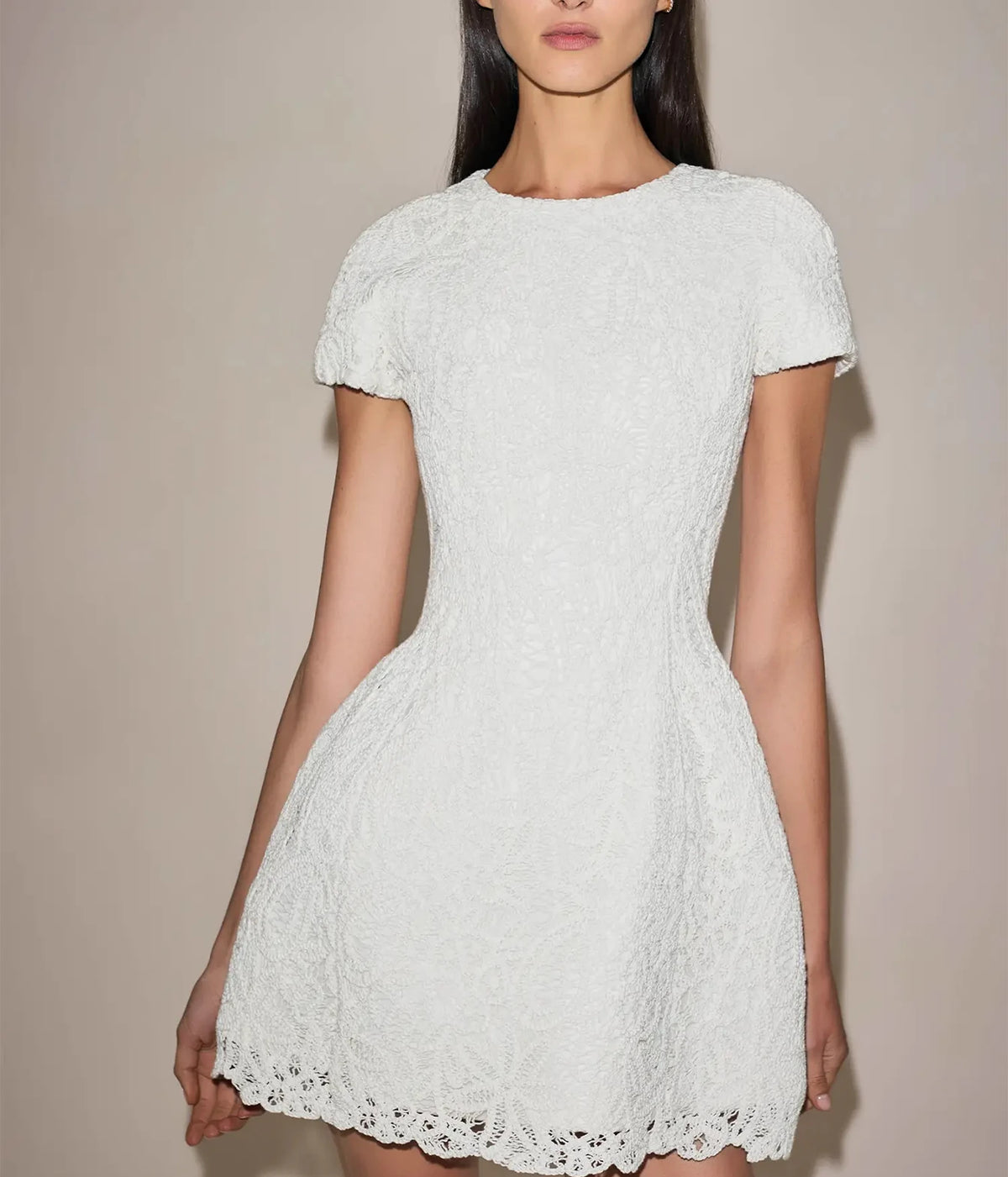 Front view of a model wearing the Alexis Regatta Dress In Floral Macrame with her gaze lowered, showing the round neckline and scalloped lace hem