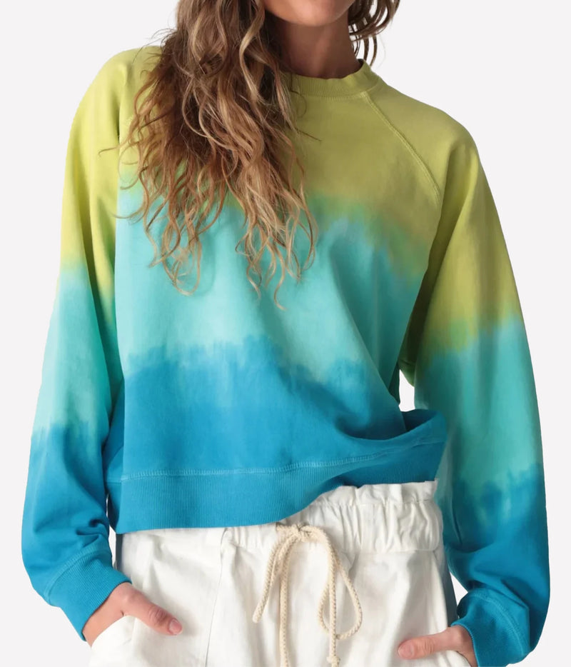Close-up front view of a model wearing the Electric Rose Ronan Ombre Sweatshirt in Chartreuse Multi, showing the chartreuse-to-aqua-to-blue ombre, crew neck, raglan sleeves and ribbed hem, with white drawstring shorts