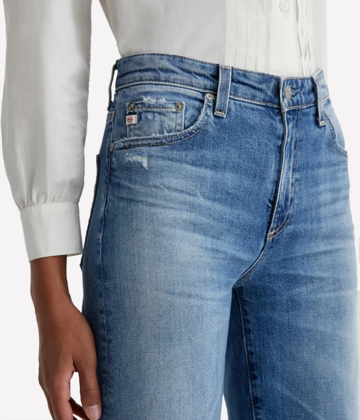 Blue jeans worn by a person with a white shirt on a light gray background