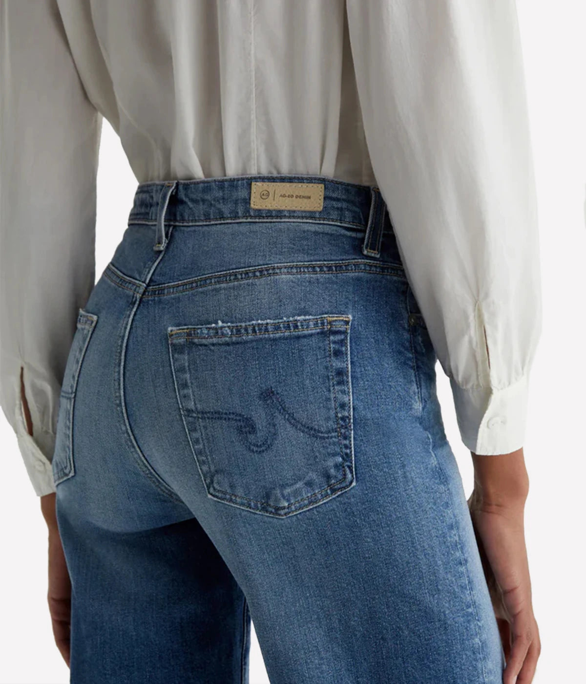 Person wearing blue jeans with a visible brand label on a white background
