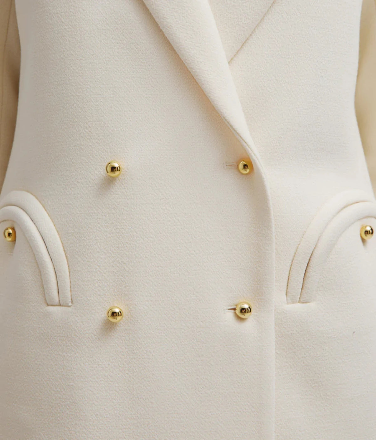 Close-up of the BLAZÉ Milano Resolute Everyday Double-Breasted Blazer in Cream showing the golden buttons and curved smiley pockets