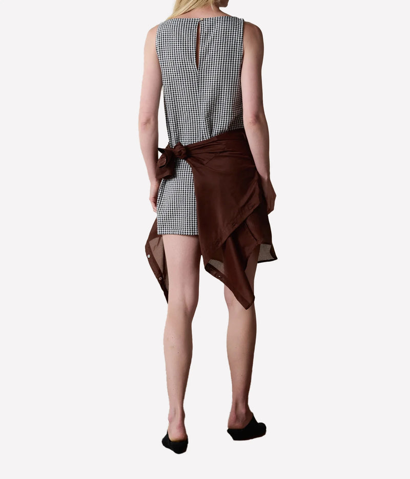 A model shown from the back wearing a sleeveless black and white gingham mini dress with a brown asymmetrical wrap skirt tied at the waist.