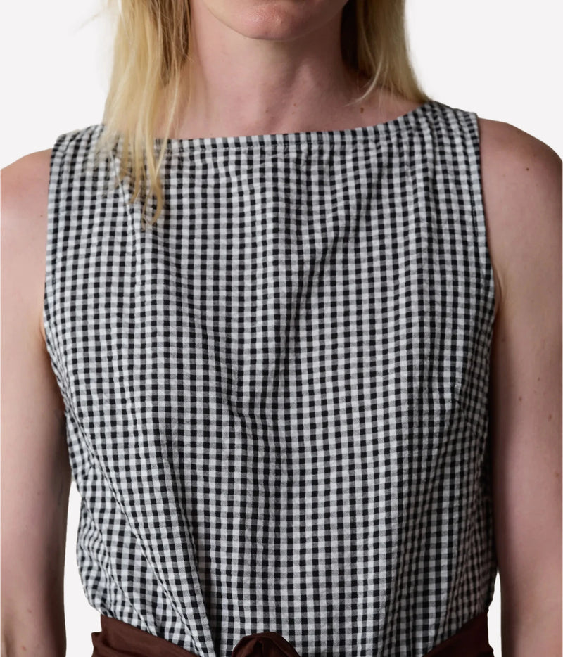 A close-up of a model wearing a sleeveless black and white gingham check top, showing the chest, shoulders, and upper torso against a plain light background.