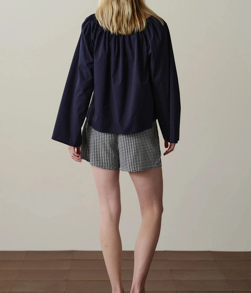 Model wearing navy gingham check shorts with a navy long-sleeve top, back view.