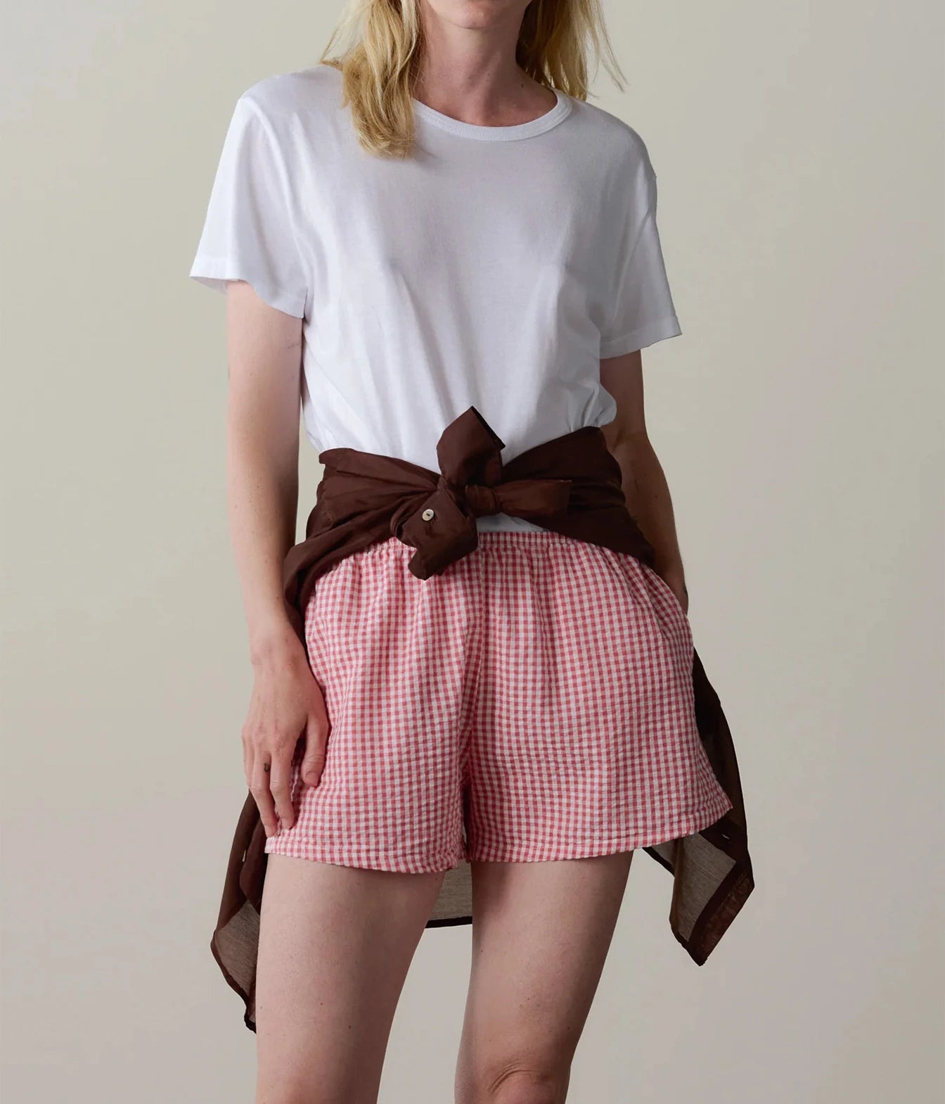 Model wearing pink gingham check shorts with a white t-shirt, front view showing the relaxed fit.