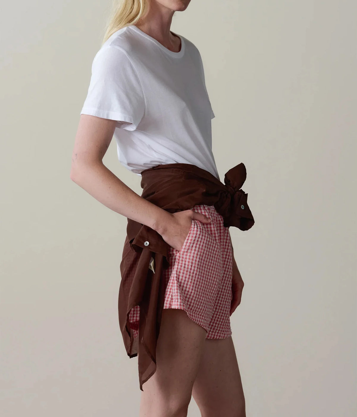 Model wearing pink gingham check shorts with a white t-shirt, side profile view showing the relaxed fit.