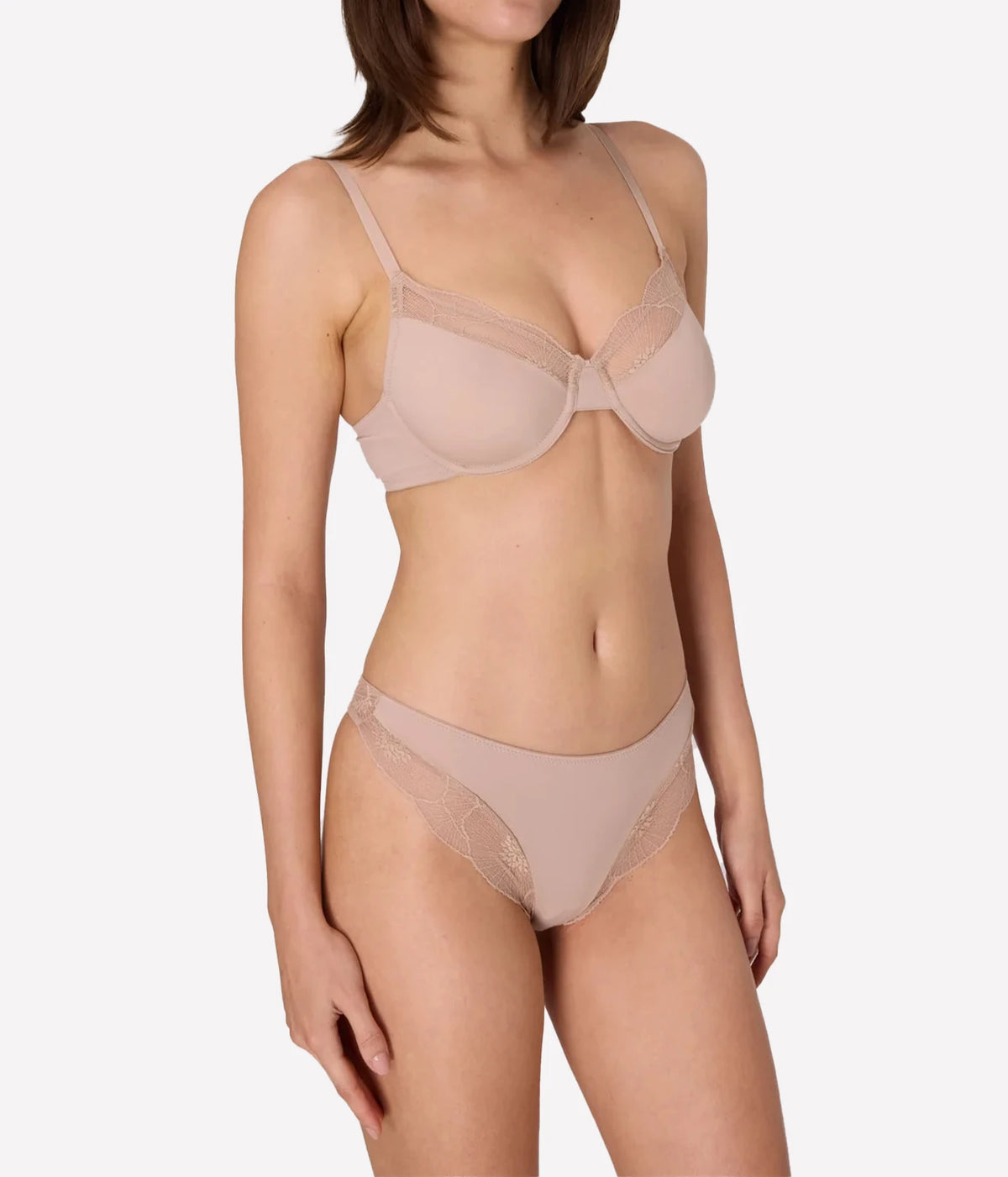 A model wearing a matching beige/nude lingerie set with a sheer lace bra and coordinating panties, Anemone Underwire Bra In Nude