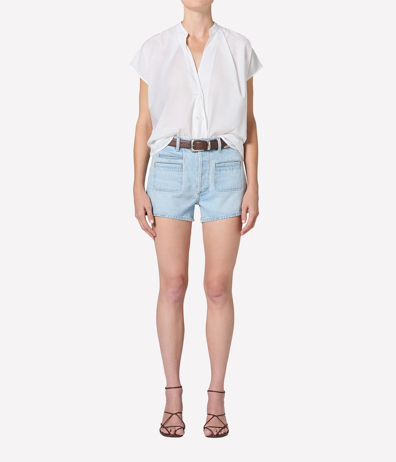 Full-length front view of a model wearing the Citizens Of Humanity Marlow Welt Pocket Short in Lasso with a white short-sleeve blouse tucked in, a brown leather belt and dark strappy heeled sandals