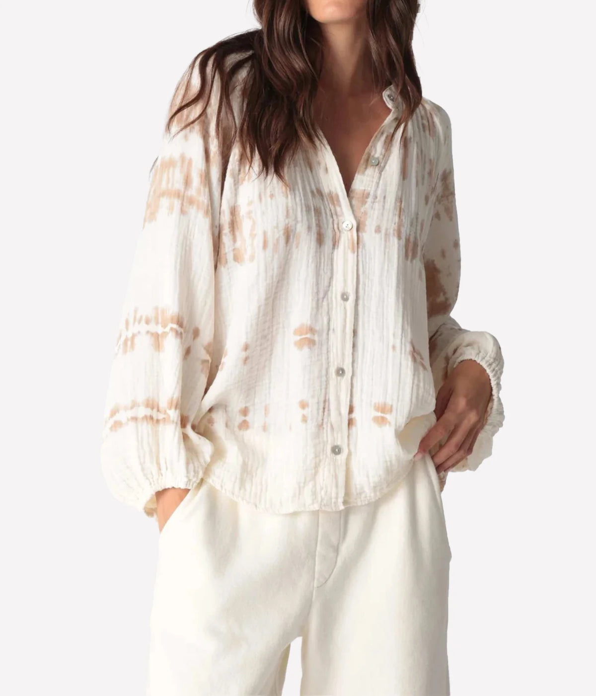 Front view of a model wearing the Electric Rose Winnie Horizon Shirt in Dune Ivory buttoned, with a hand in her pocket, showing the band collar, ivory crinkle gauze with dune tie-dye marks and balloon sleeves, with ivory trousers