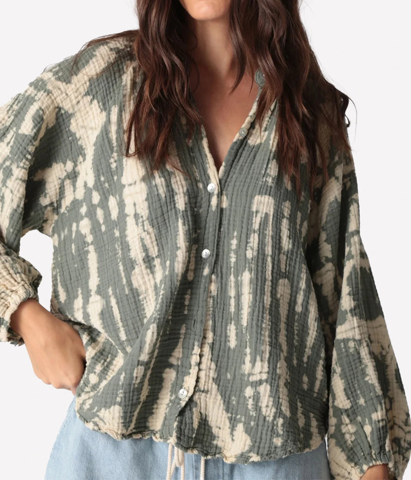 Close front view of a model with a hand on her hip in the Electric Rose Winnie Horizon Shirt in Moss Ivory buttoned, showing the moss and ivory tie-dye crinkle gauze, V neckline, shell buttons and gathered cuffs, with light-wash denim