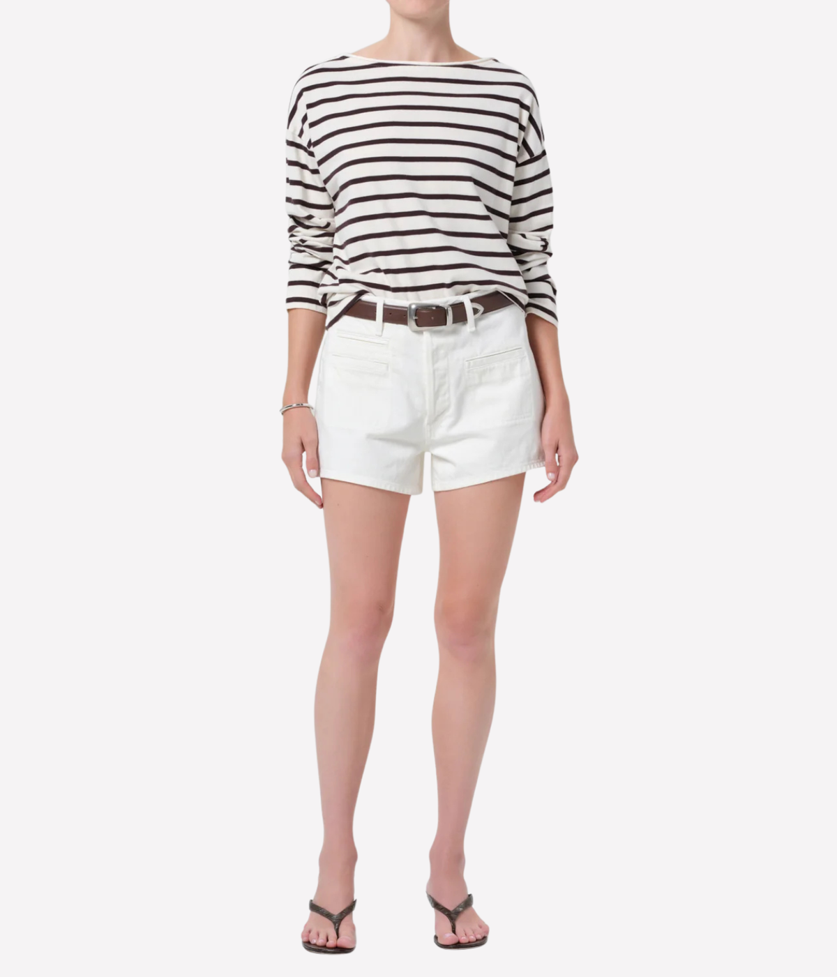 A model wearing a black and white horizontally striped long-sleeve top, white denim shorts, a brown leather belt, and black flip-flop sandals, photographed against a solid white background.