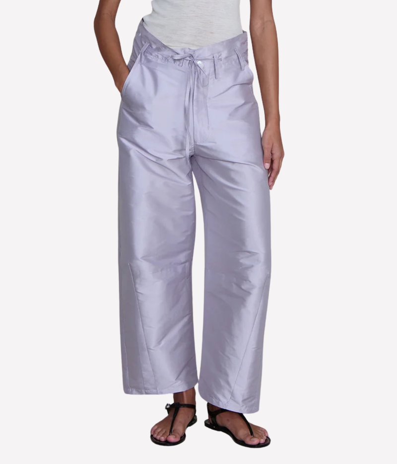 Close-up front view of a model wearing the Chan Luu Techno Taffeta Barrel Pant in Lilac with a grey marl top and black thong sandals, showing the tied front waist, button closure and curved barrel legs
