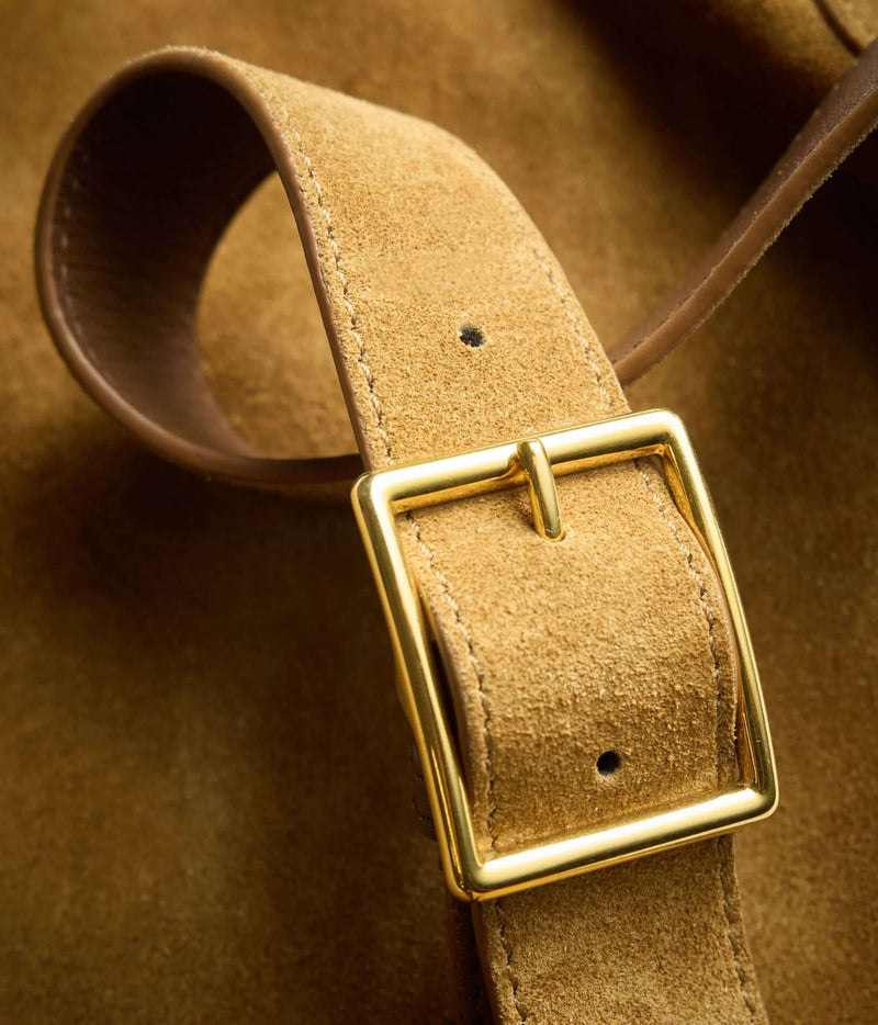 A close-up of a tan suede belt with a polished gold-tone metal buckle, resting on a matching brown suede background.