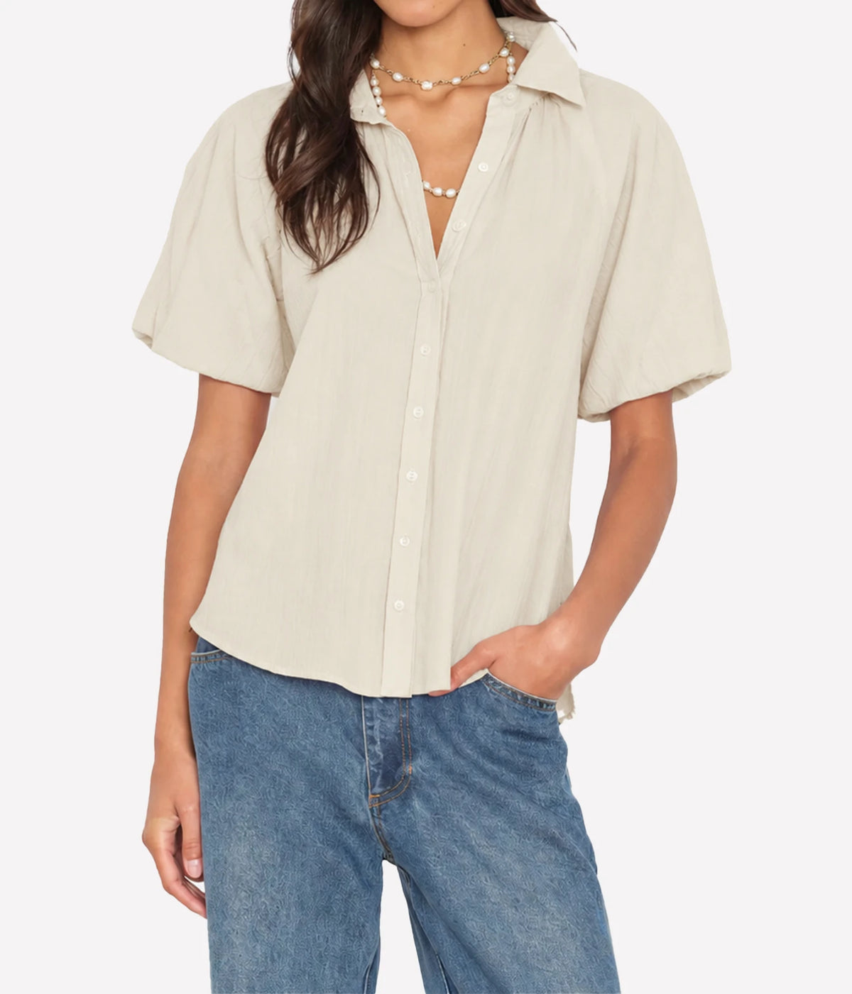 Model wearing the Xirena Lyla Shirt in Parchment open at the neck over mid-wash blue jeans, with a pearl beaded necklace and one hand in her pocket